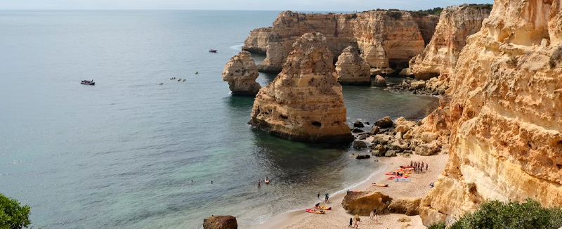 aerial view of a rocky beach in the Algarve with people on the sand and two boats in the sea