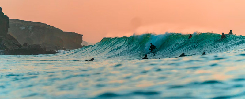 Three people surfing a wave at the end of the day.