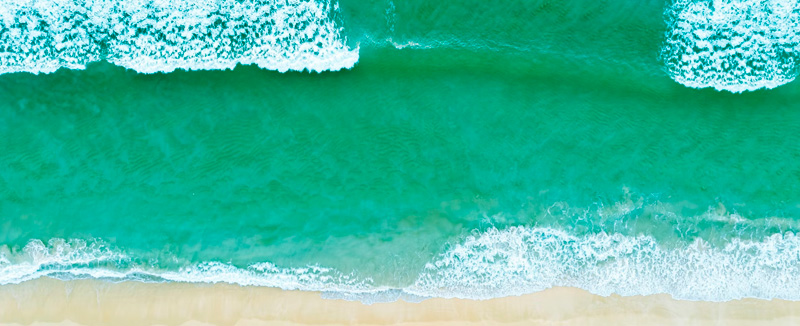 vista de drone de praia com o mar esverdeado e claro e ondas a rebentas e areia dourada
