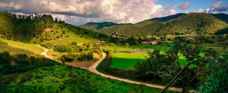 vista de um vale com bastante vegetação verde cercado por montanhas sob um céu nublado