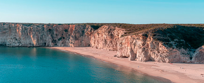 Aerial view of Sagres Beach with the calm blue sea, sand, and rocky mountains during the day