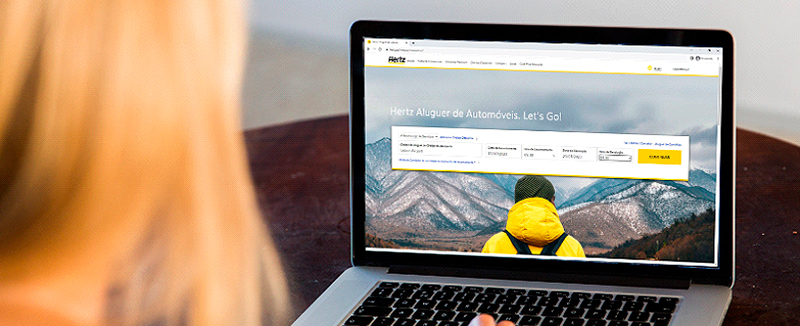 pessoa loira sentada em frente a computador a realizar aluguer de viatura no website da Hertz
