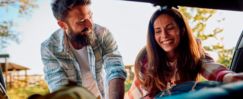 view from inside the boot of a car showing a smiling man and woman handling suitcases