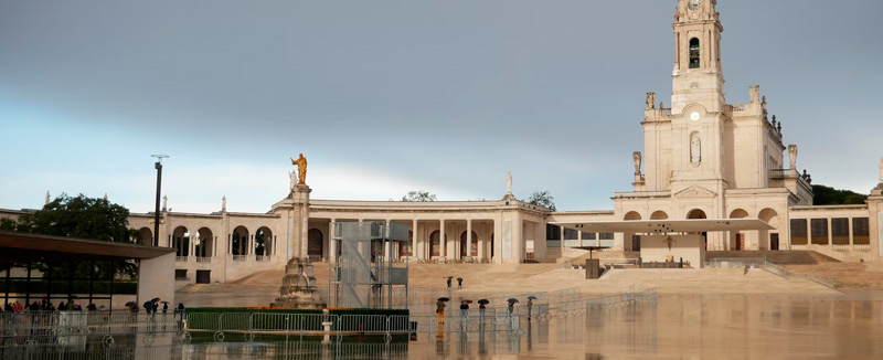 recinto do santuário de Nossa Senhora de Fátima num dia chuvoso com edifício alto com sino no topo