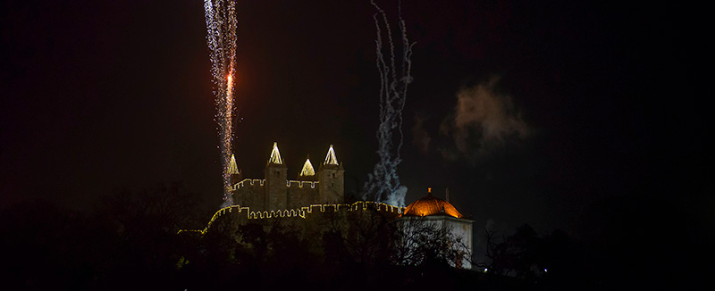 castelo de santa maria de feira num dia à noite iluminado com luzes natalinas e com fogos de artifício 