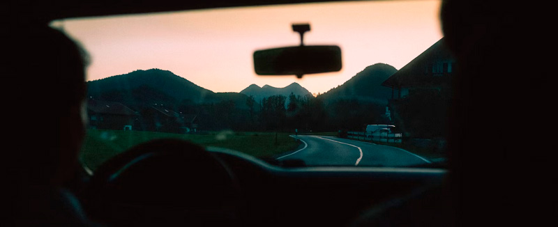 view from inside the car showing two people driving, with mountains and a sunset in the background