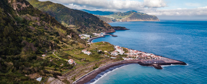 vista aérea da praia do fogo onde se mostra o mar azul-claro a encontrar-se com a areia preta da praia