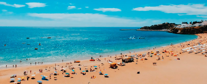 pessoas numa praia em albufeira num dia de verão com mar calmo e azul