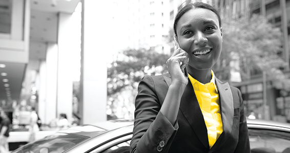 Grey scake image of a Woman in a yellow shirt talking on the phone with the top of a car in the background