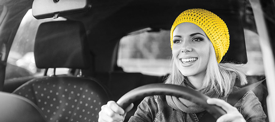 A woman in her early 20s wears a yellow beanie and smiles as she sits in the driver’s seat of a rental car.